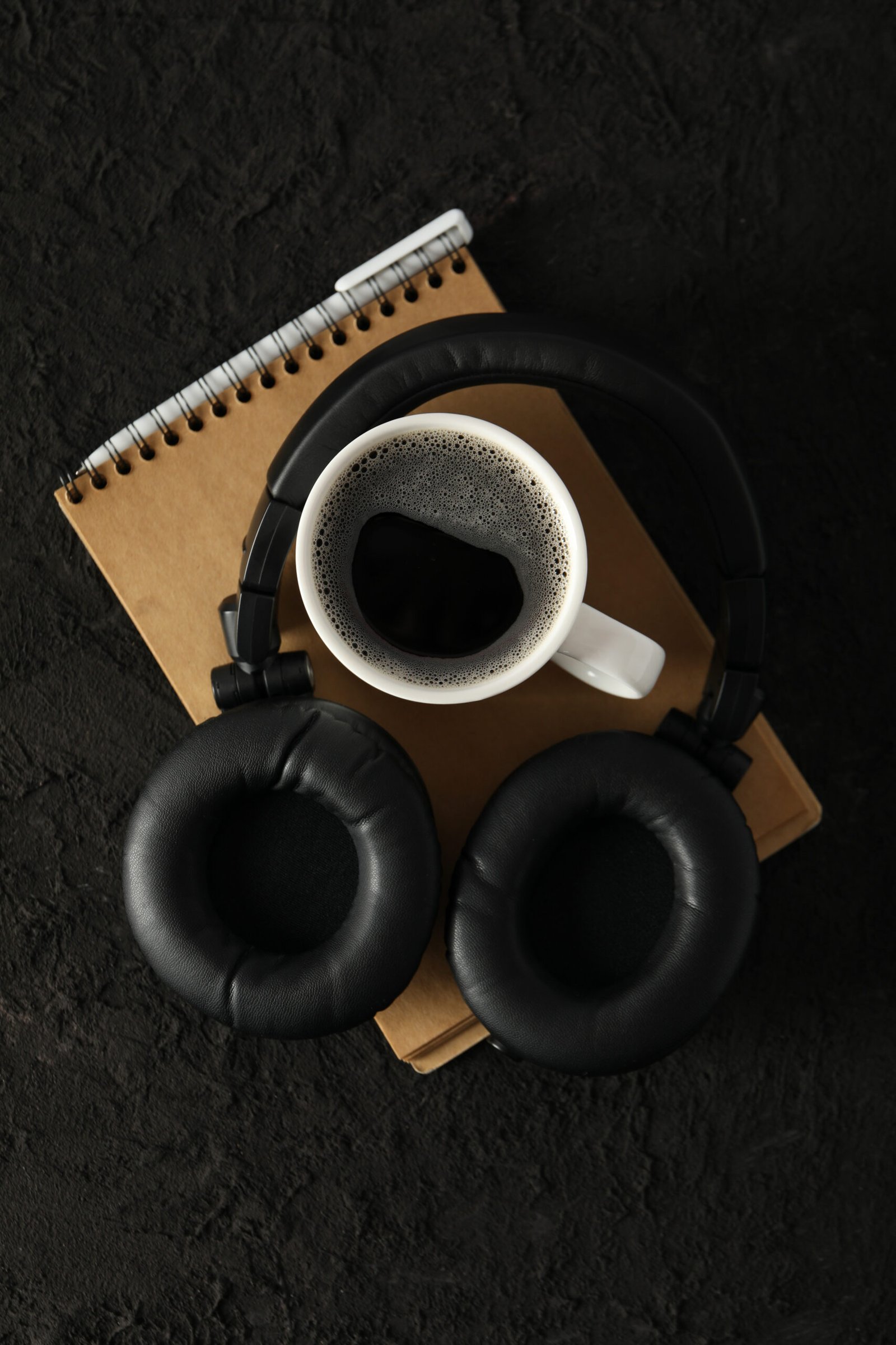 A cup of coffee with black headphones on a dark background